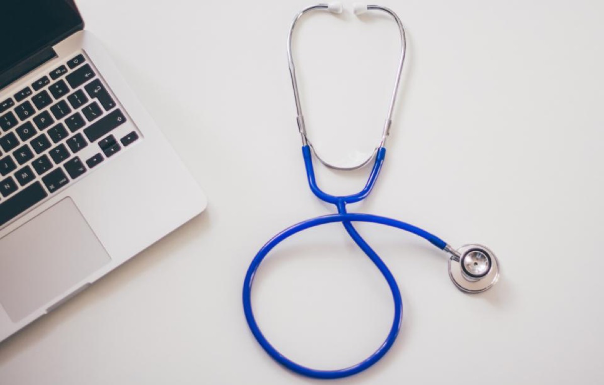A laptop and a stethoscope on a desk, representing an online consultation